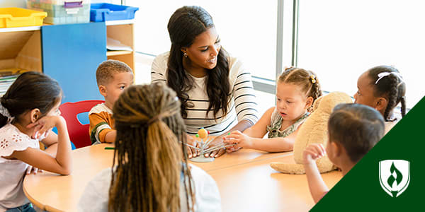 Female teacher sits at a small table showing children a model of the solar system