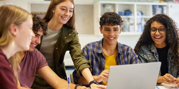 Smiling high school students gathered around a laptop
