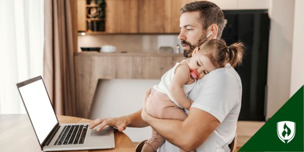 A father holds his baby while working through an online accounting program at home