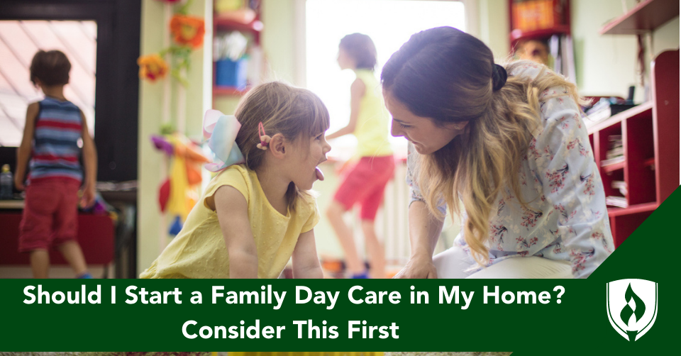 A day care provider plays with a little girl in a yellow shirt as other kids play in the background of her living room