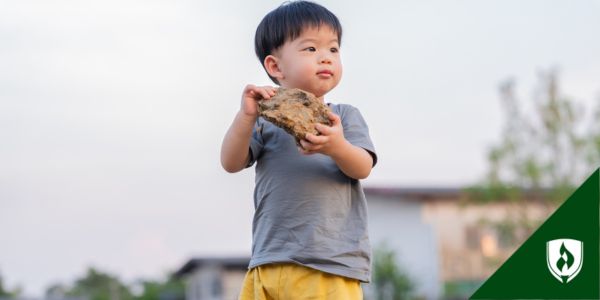 An adorable toddler holds a big rock with both hands
