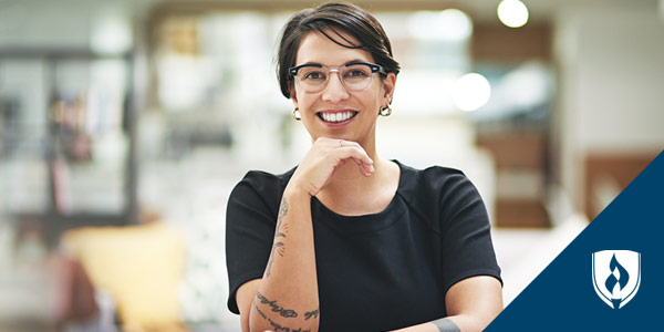 smiling woman with glasses sitting at table with hand under chin