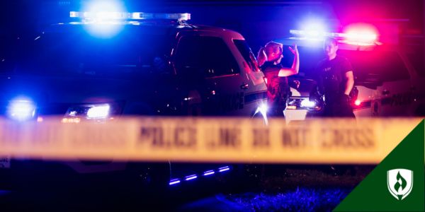 Two police officers stand in front of their vehicles at night