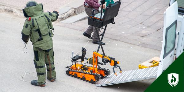 A bomb technician in full protective gear works with a bomb robot