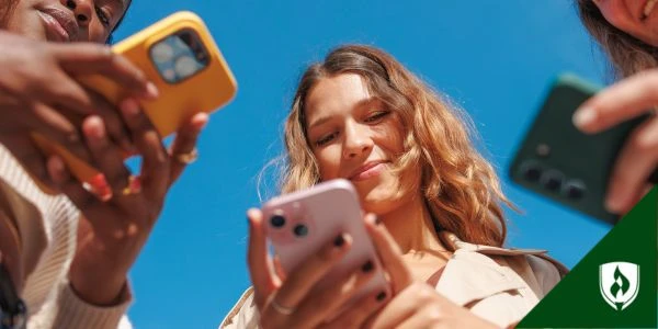 Three people look at their phones under a blue sky